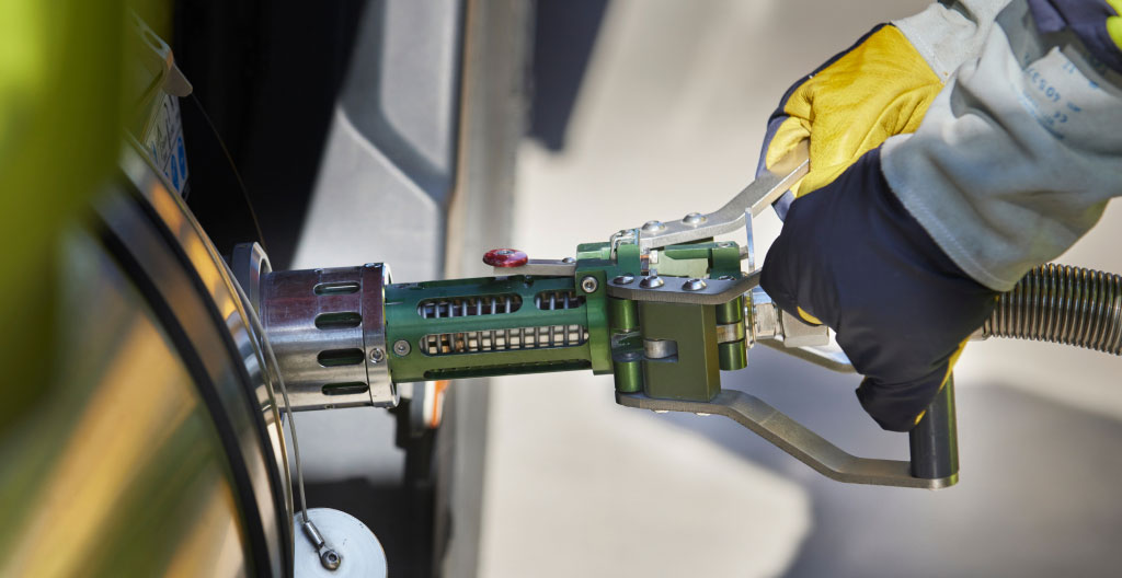 Un opérateur en vêtement de travail vu de dos ravitaille un camion depuis une borne de distribution moderne sur un site industriel français